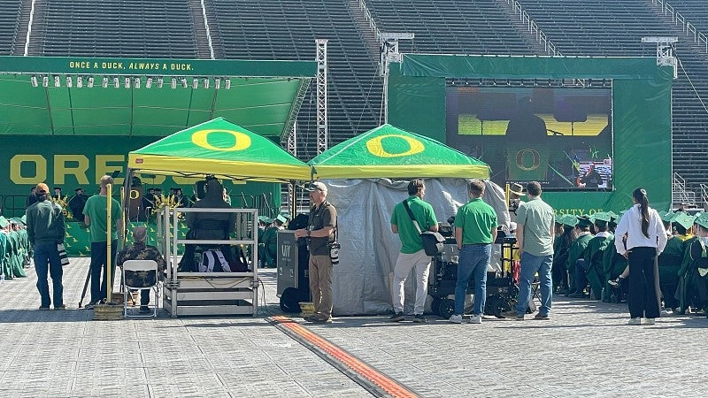 UO green and yellow tents at a commencement ceremony with photographers standing by them