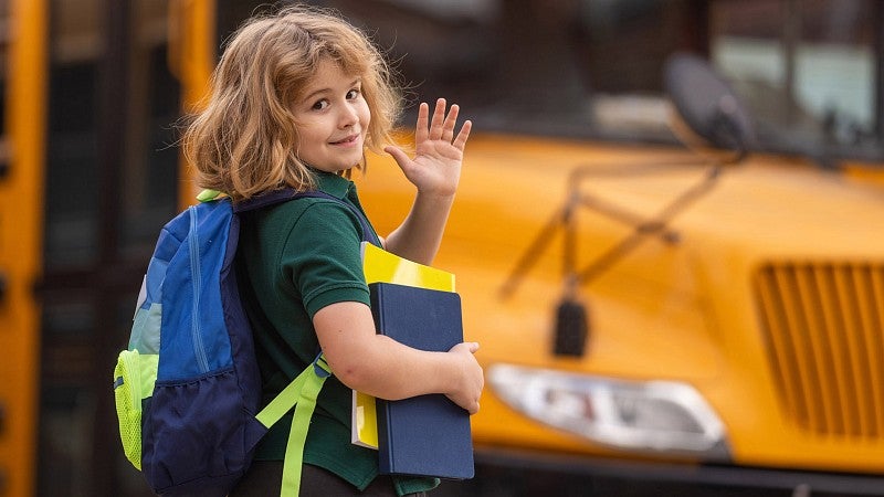 Child waving in front of school bus