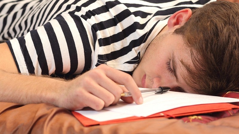 Young man asleep on top of homework papers