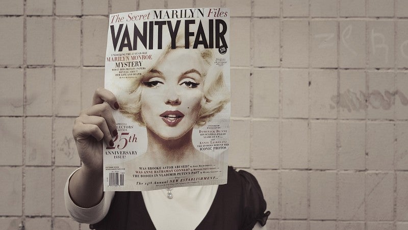 Woman holding magazine cover featuring Marilyn Monroe's face over her own face