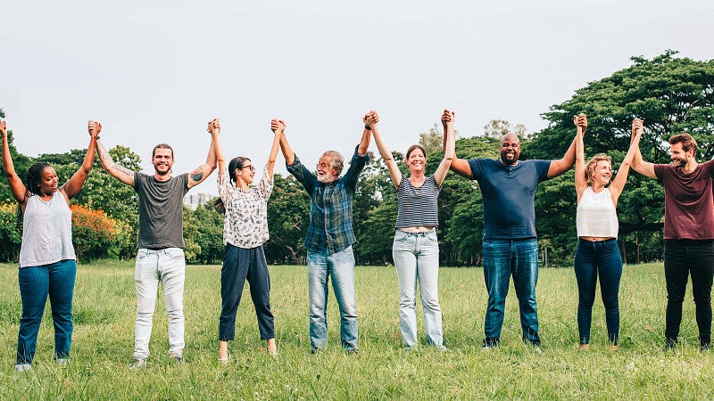 Group of adults of various shapes with arms raised and hands clasped
