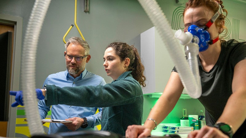 Two scientists looking at data in the lab, while a woman on an exercise bike participates in the study
