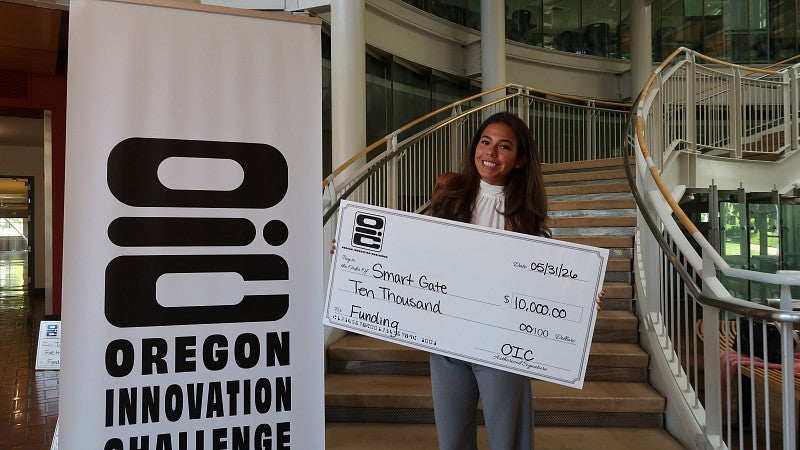 A student poses with a large check for funding through the Oregon Innovation Challenge