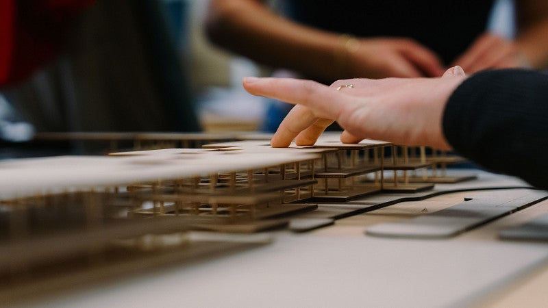 A student's hand touches a model-sized rendition of a design plan for an airport
