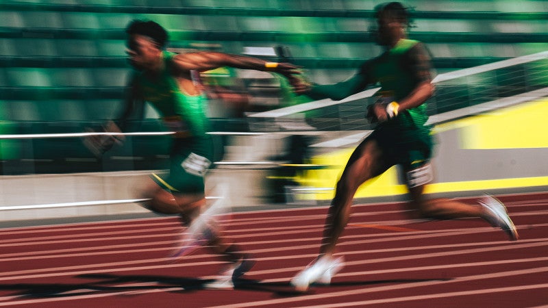 A runner passes a baton to another in a blur of motion