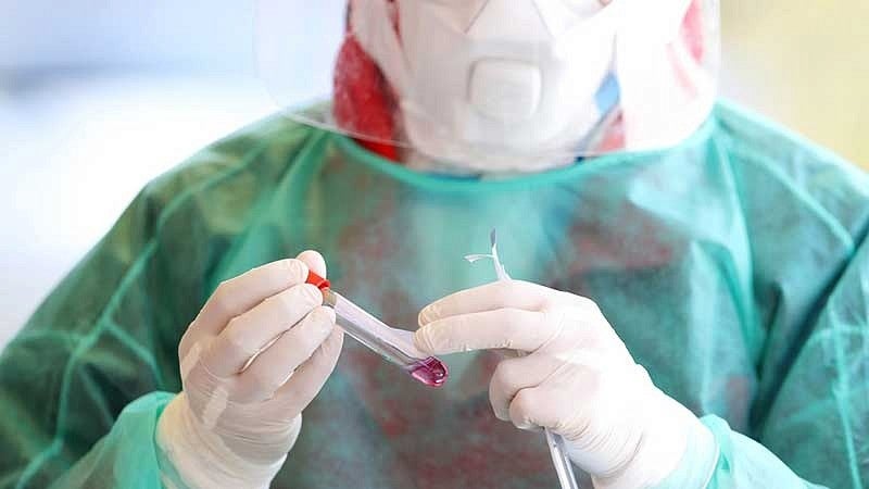 Person in protective gear holding test tube vial 