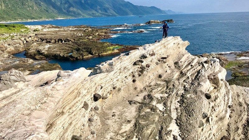 Person standing atop steep, rocky outcrop above the sea.