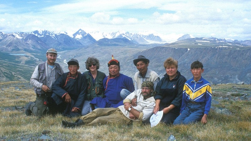Group image of Jacobson-Tepfer, Gary Tepfer, friends and assistants. In the distance are the peaks of 	Tavan Bogd separating Mongolia from Russia. Photo: Gary Tepfer.