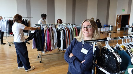 A woman stands next to a rack of clothes
