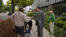 President Scholz shaking the hand of a parent during fall term move-in with a student opening a cart and Melissa Scholz watching from the side