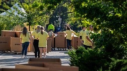 volunteers in yellow shirts helping new students move boxes into residence halls