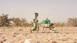 Girl pushing wheelbarrow with water containers in dry landscape