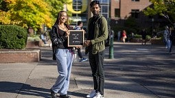 two students in front of the Lundquist College of Business holding a sign that says First Day of School Go Ducks!!