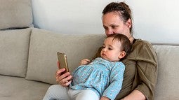 Mother looking at cellphone while holding baby on her lap