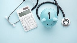 A stethoscope with a white calculator and light blue piggy bank displayed together