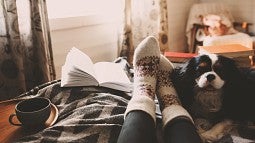 person on couch with book and dog