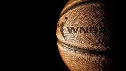 Basketball with WNBA logo emerging from black background