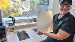 Custodian Judy Haines displays a metal garbage cover designed and fabricated at the Knight Campus