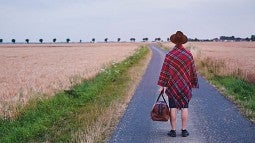 Woman holding valise standing in road looking away