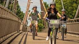 young adults ride bikes over a bridge on a sunny day