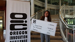 A student poses with a large check for funding through the Oregon Innovation Challenge