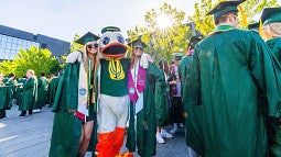 Graduates in gowns pose with the Duck (photo: Travis Worrell, Student Services and Enrollment Management)