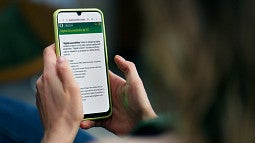 A person holds a smartphone reading a page about digital accessibility at the UO