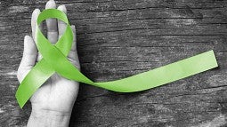 A hand holding a green ribbon, a symbol of mental health.