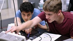 Image shows two students in the internship program at work in a UO optics lab