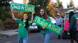 Two students, wearing green, hold signs that say "Once a Duck," "Always a Duck" 