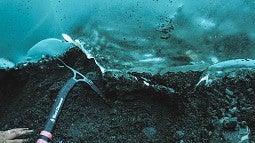 Meyer reaches with an ice axe on frozen sediment beneath a glacier in Alaska