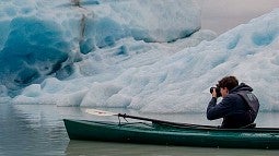 Man in a kayak taking a photo of a glacier