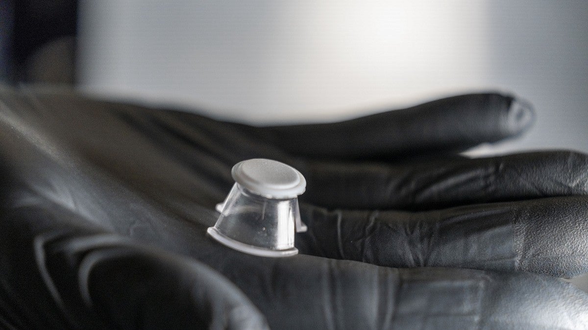 Close up view of a white disk in the palm of a hand clad in a black glove