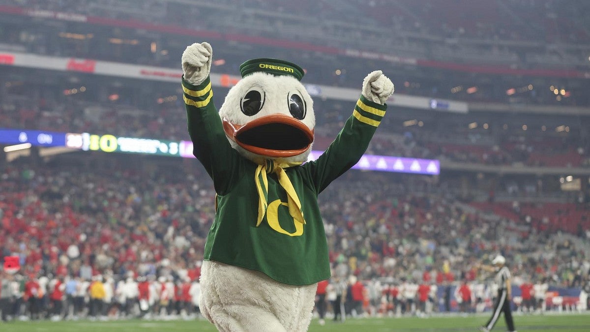 The Duck walking across a football field with his arms raised overhead to a cheering crowd