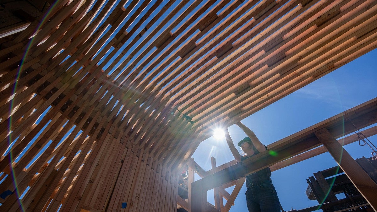 A student installing a section of the new home's roof supports during the Bruton Design Intensive