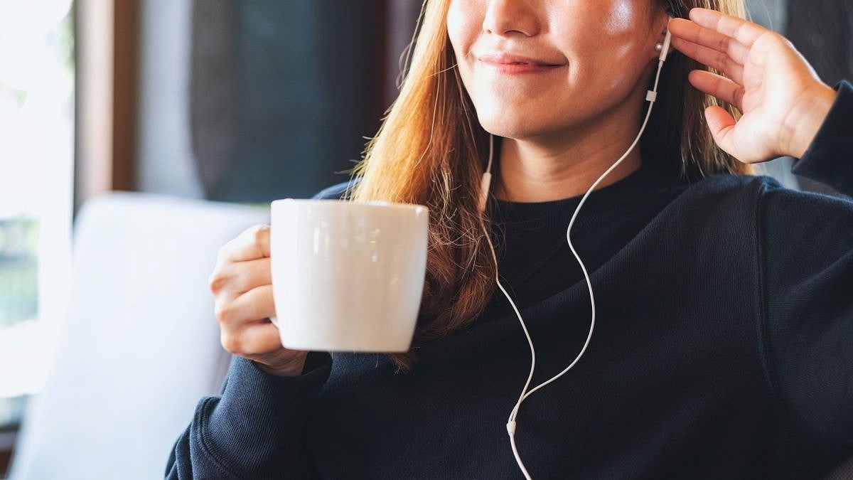 woman with long brown hair wearing ear buds and holding coffee cup 