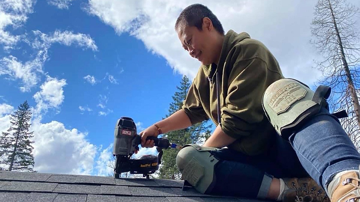 Haisu Huang nailing shingles on the roof of a tool shed built for a fire survivor