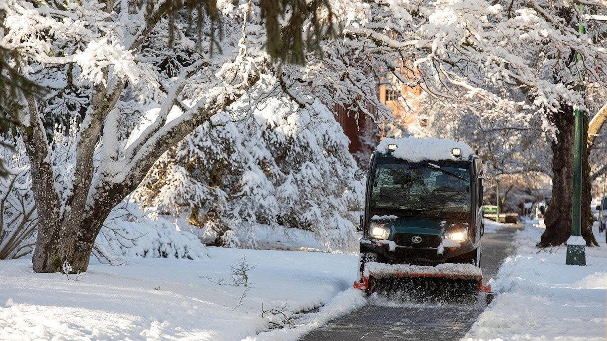 a driver plows snow from a sidewalk on a winter day