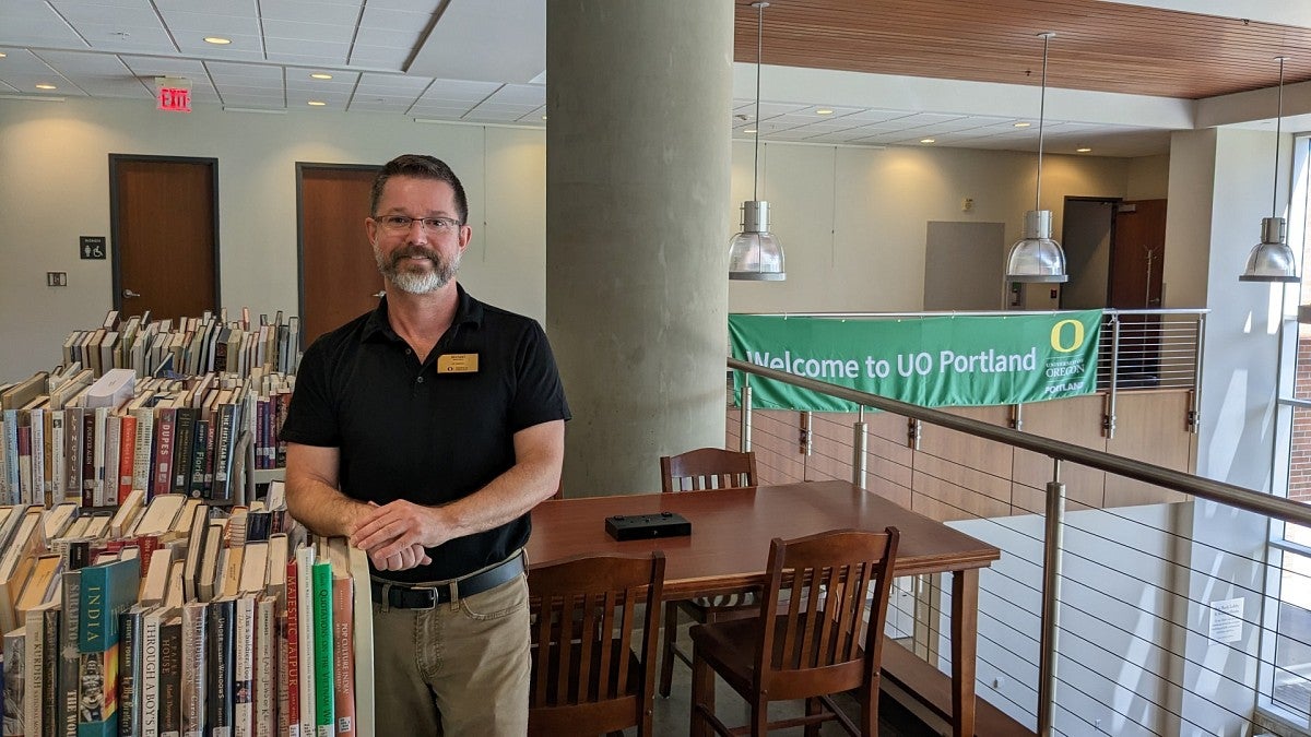 Michael Brown next to carts of books in UO Portland Library.