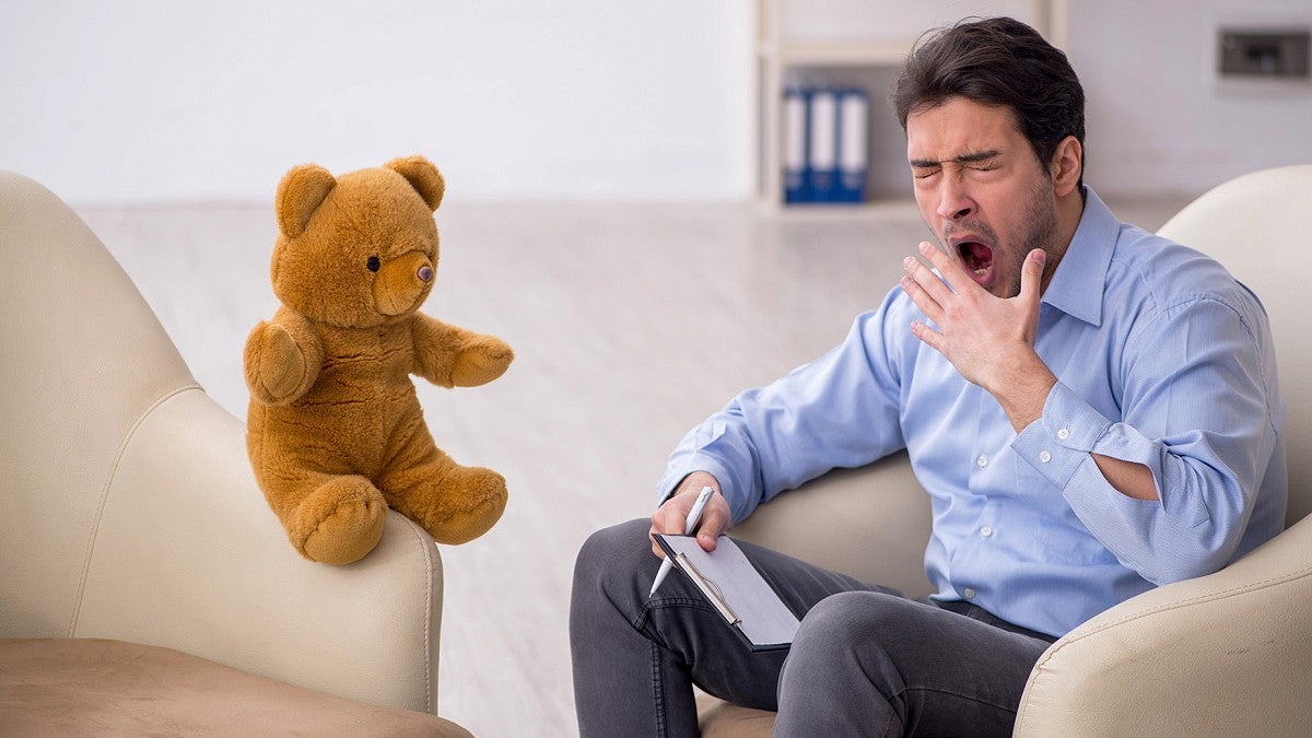 Bored therapist yawning next to teddy bear patient