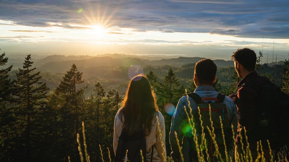 three people standing on a summit watching the sunrise