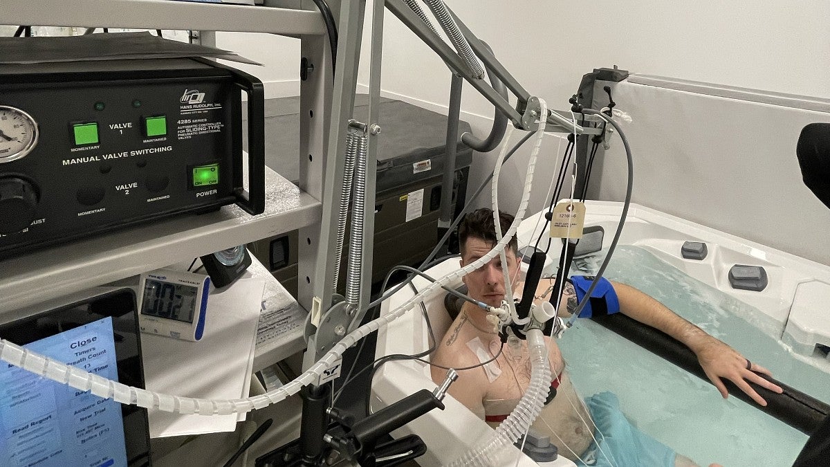 A man sits in a hot tub connected to test equipment in a university laboratory