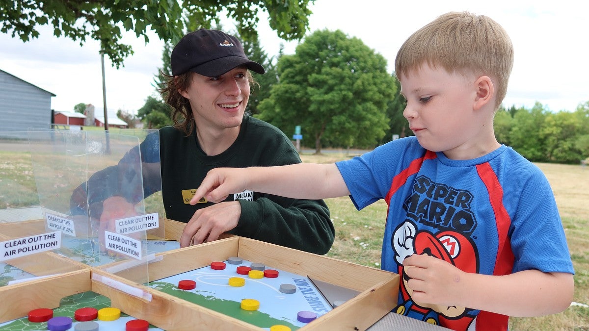 A museum outreach educator smiles as a boy points to a spot on a board game about protecting the environment