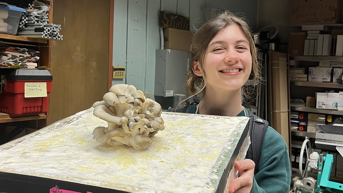 Smiling woman holding a panel of insulation material with mushrooms growing on top
