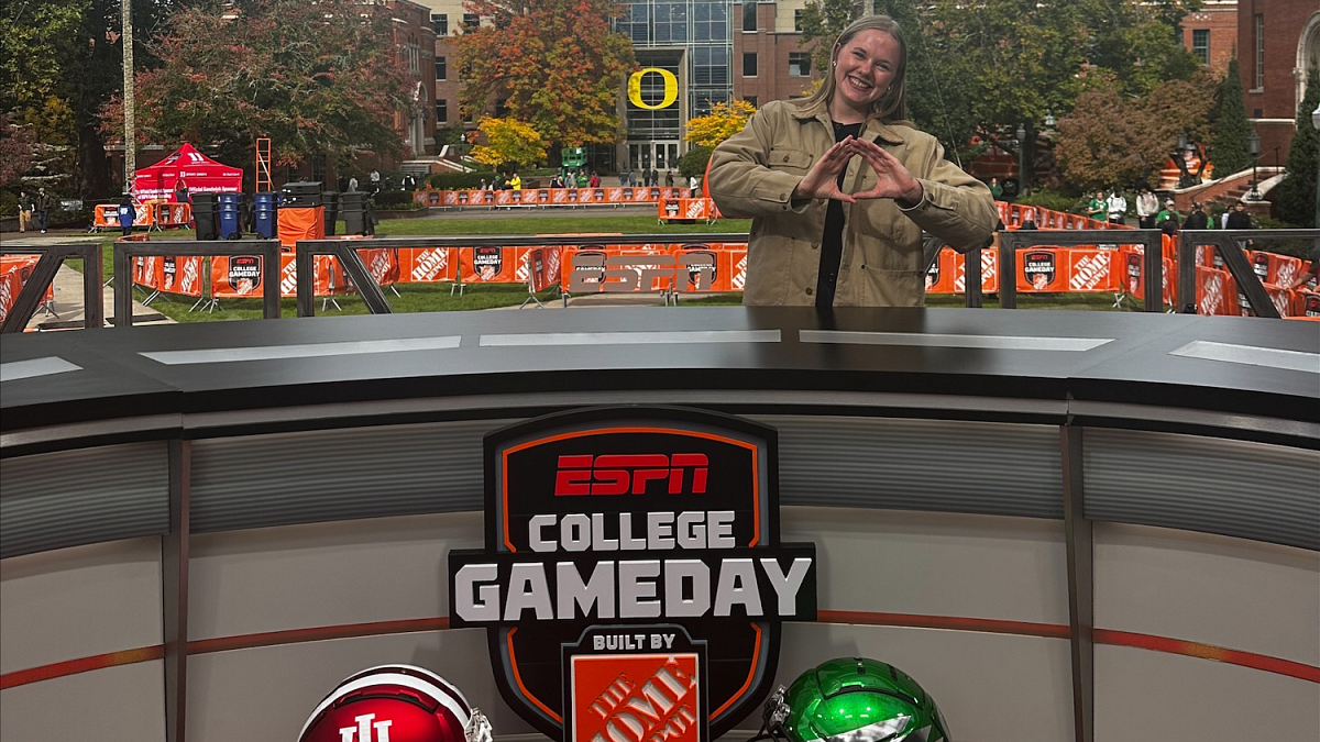 A student sitting behind the desk at the College GameDay set throws an O