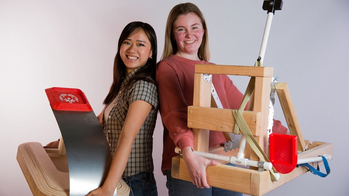 Students holding two prototypes of a cornhole game for Special Olympians