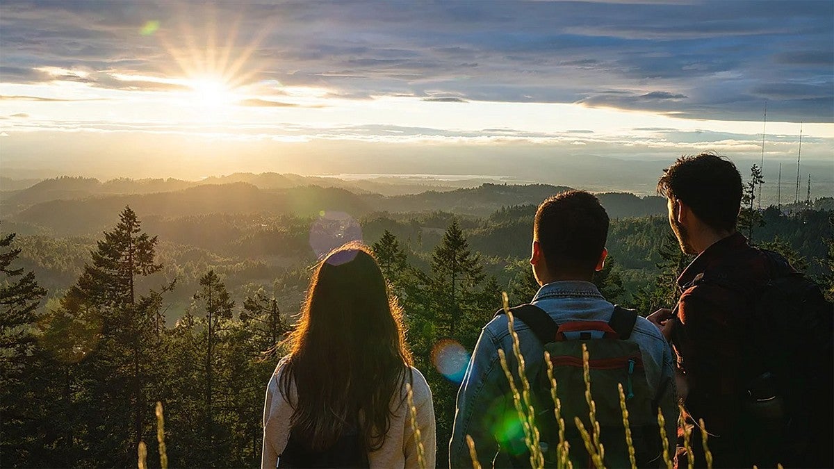 Three people watching a sunset from a hilltop