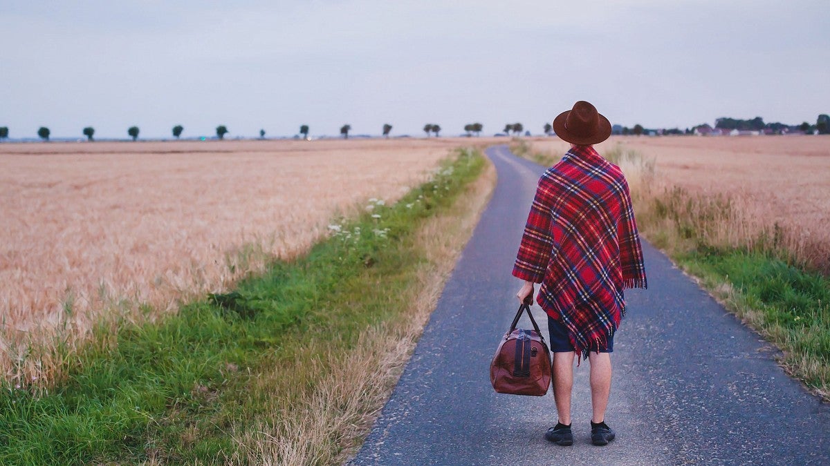 Woman holding valise standing in road looking away