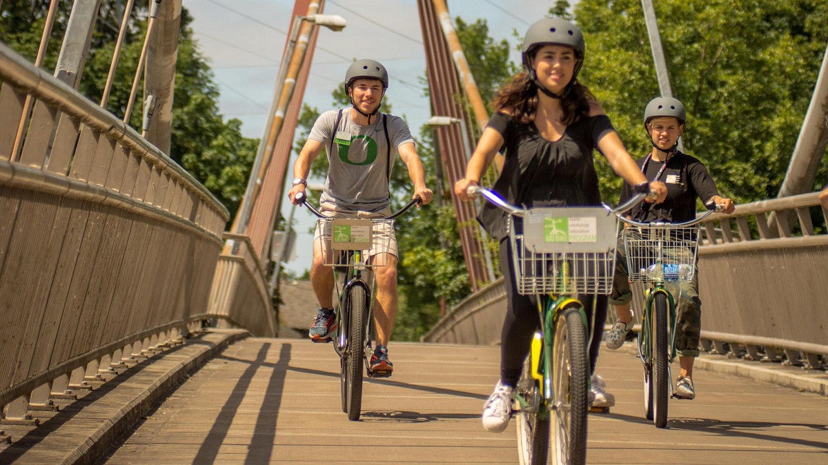 young adults ride bikes over a bridge on a sunny day