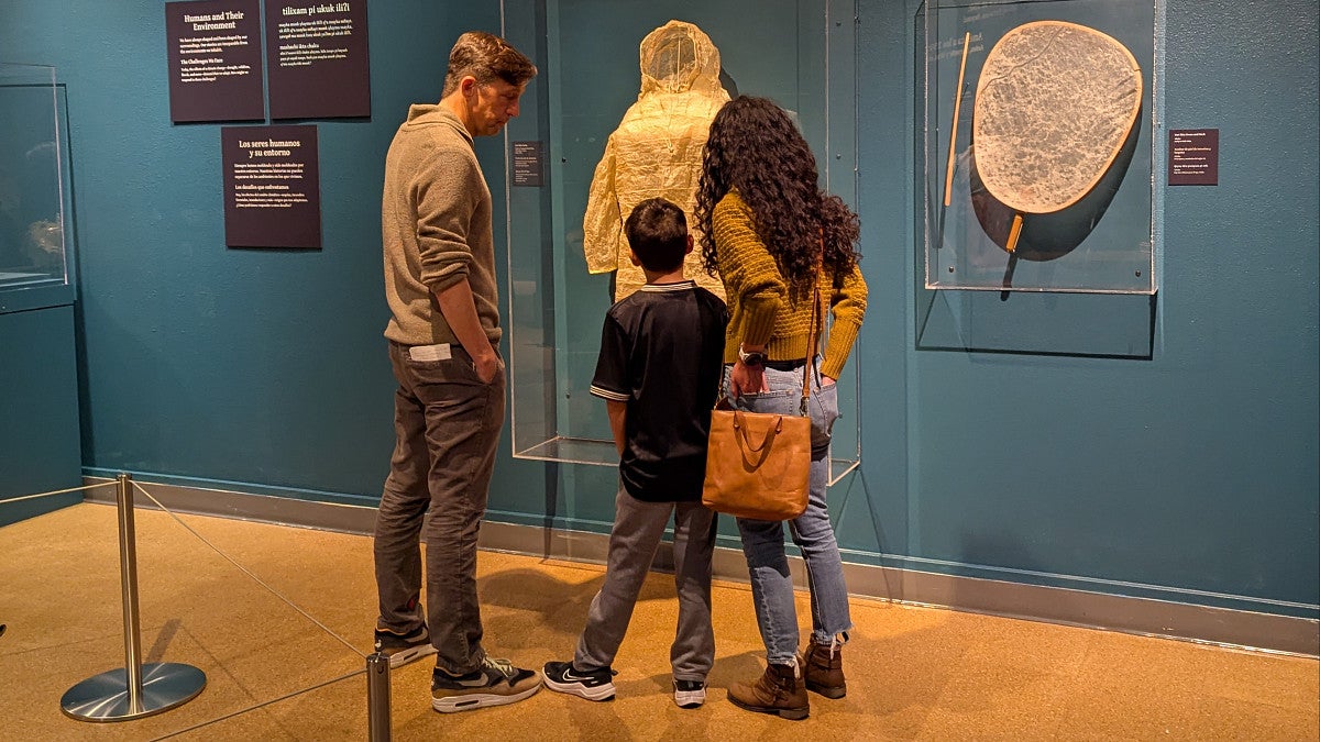 A man, woman and child view a Native parka in a museum